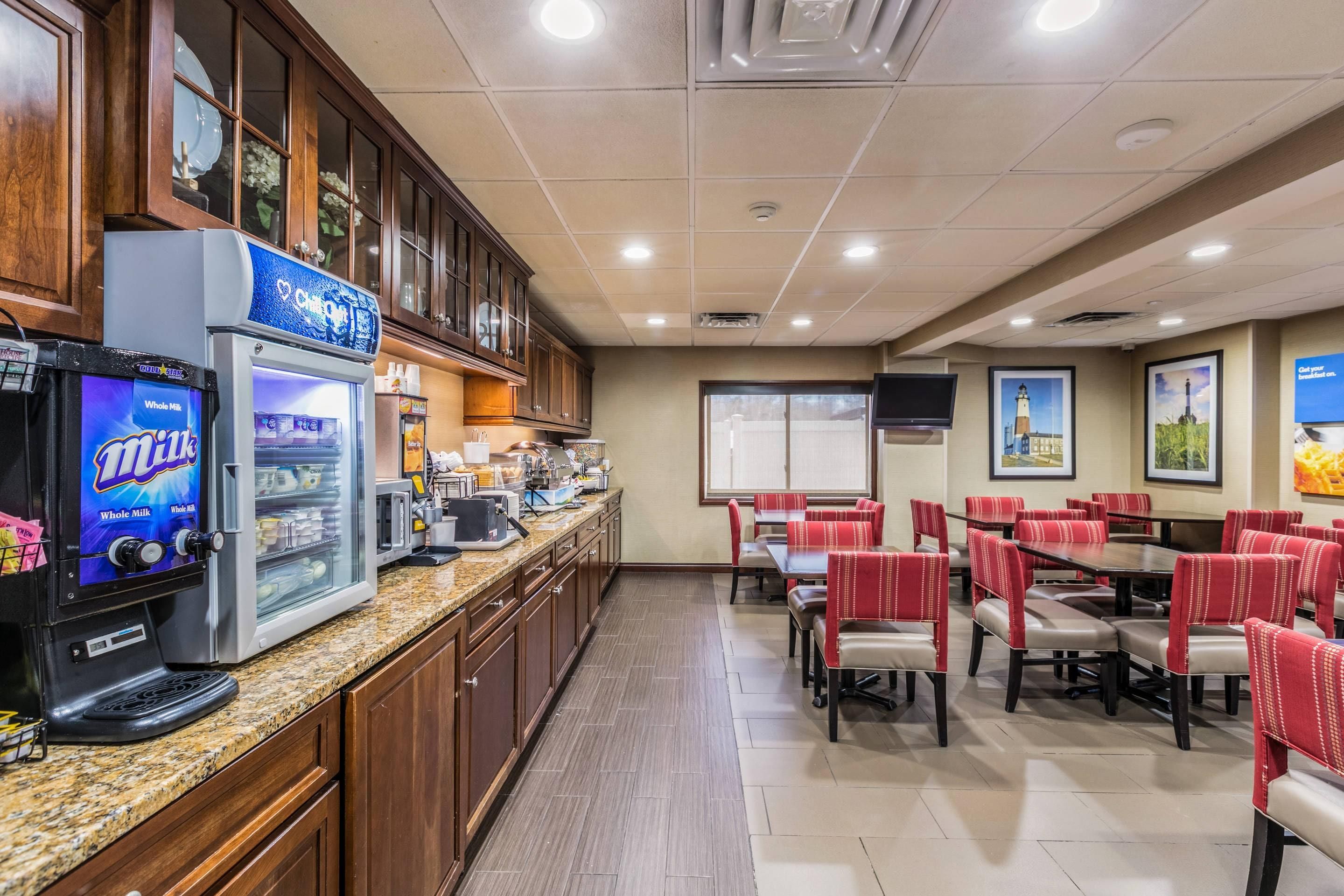 Uma área de refeições de hotel com uma máquina de café de leite integral, um refrigerador e uma tela de televisão.