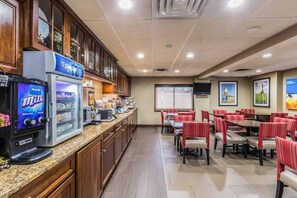 A hotel dining area with a whole milk coffee machine, a refrigerator, and a TV screen. - Comfort Inn Medford - Long Island (Medford)