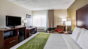 A hotel room with a bed, a desk with a television, a chair, a desk lamp, and a window with curtains.