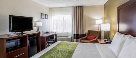 A hotel room with a bed, a desk with a television, a chair, a desk lamp, and a window with curtains.