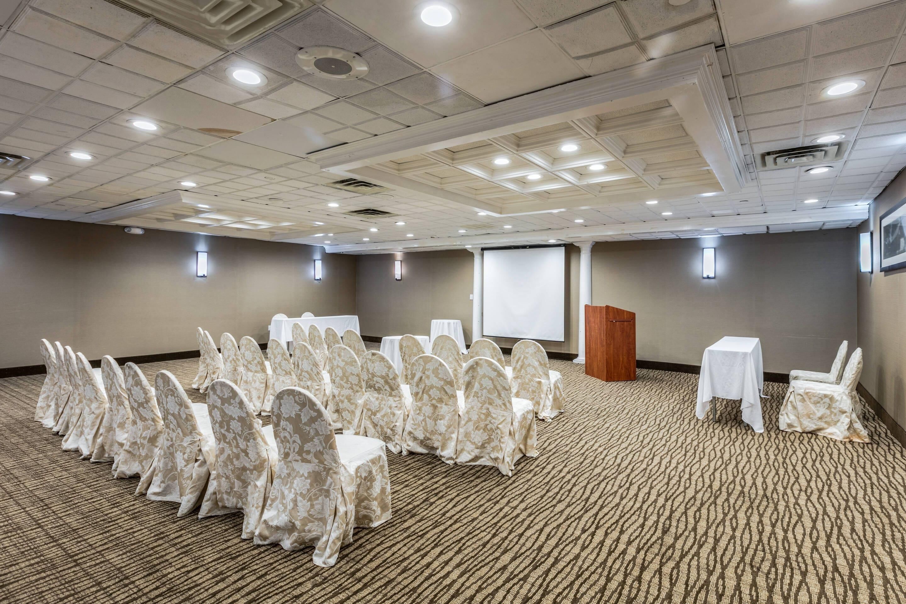 A conference room with rows of chairs, a podium, and a projector screen.