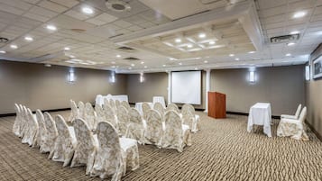 Une salle de conférence avec des rangées de chaises, un pupitre et un écran de projection.