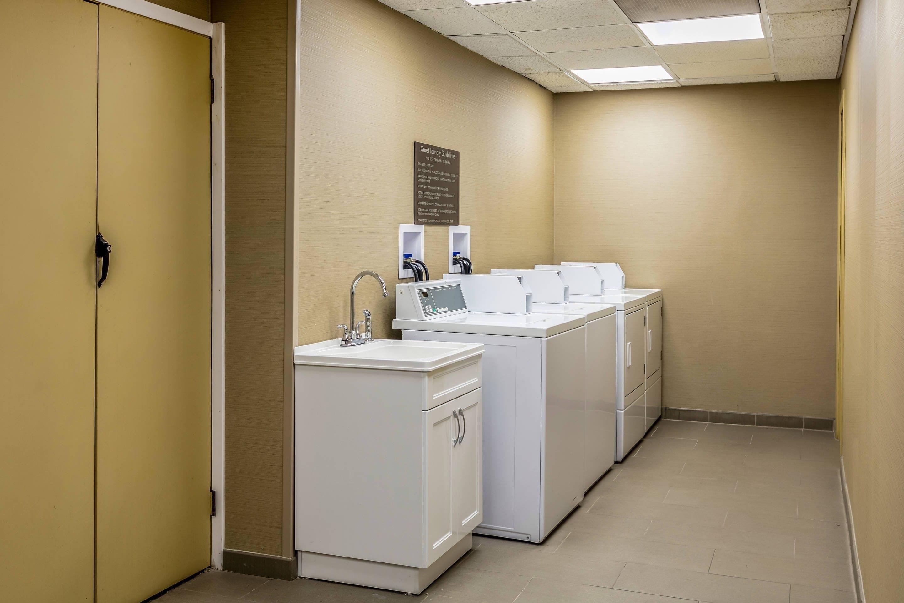 A hotel laundry room with a sink, a washing machine, and a dryer.