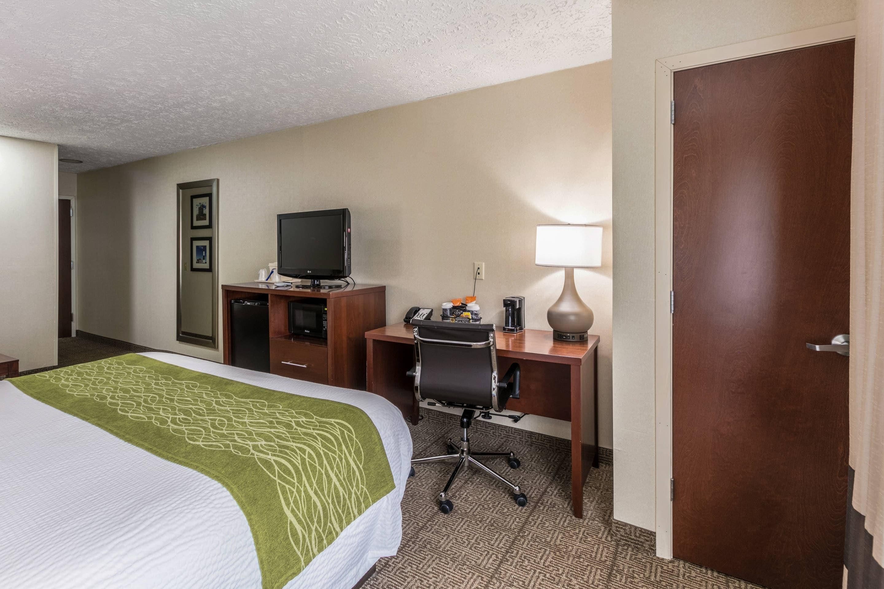 Una habitación de hotel con una cama, un escritorio con computadora, un televisor y una lámpara.