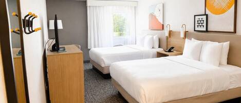 Une chambre d’hôtel avec deux lits, un bureau, une chaise, un téléphone et une fenêtre avec des rideaux.