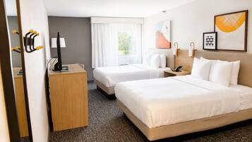 A hotel room with two beds, a desk, a chair, a telephone, and a window with curtains.