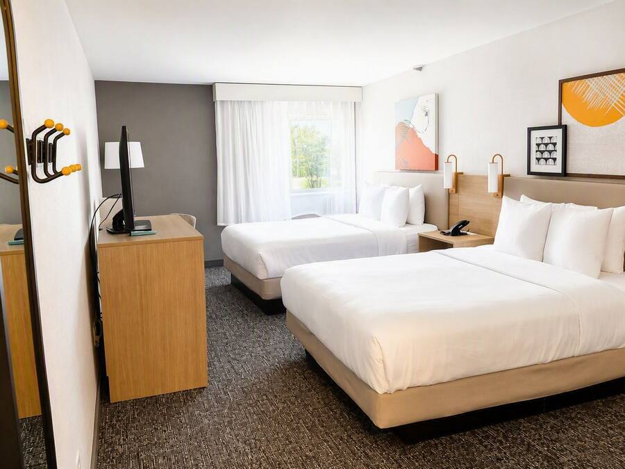 A hotel room with two beds, a desk, a chair, a telephone, and a window with curtains.