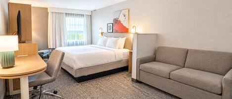 Una habitación de hotel con cama, sofá, escritorio con lámpara y una silla.