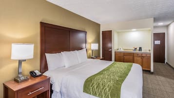 A hotel room with a bed, bedside lamps, a desk with a phone, a mirror, and a kitchenette.