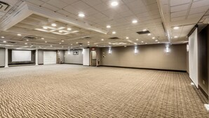 Une grande salle de conférence, recouverte de moquette, avec un plafond haut et des luminaires encastrés.