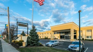 A hotel entrance with an American flag, a parking lot, and a sign for a nearby Marriott hotel. - Comfort Inn Medford - Long Island (Medford)