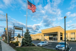 A hotel entrance with an American flag, a parking lot, and a sign for a nearby Marriott hotel. - Comfort Inn Medford - Long Island (Medford)
