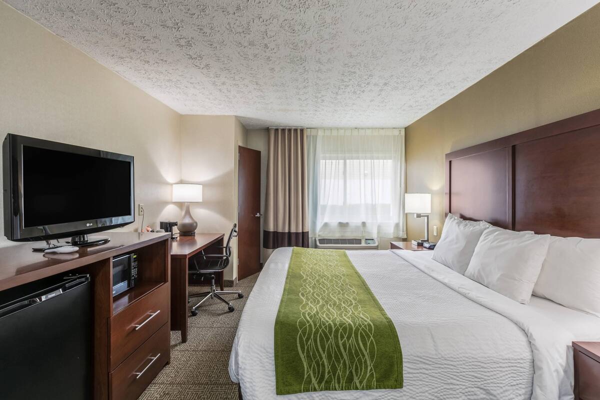 Een hotelkamer met een bed, een bureau met een televisie, een magnetron en een lamp.