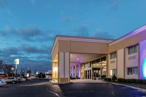 Hotel com entrada coberta, estacionamento e placa visível de um restaurante próximo.