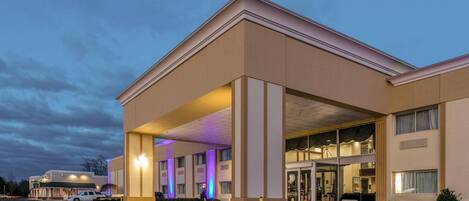 A hotel with a covered entrance, large windows, and a parking lot.