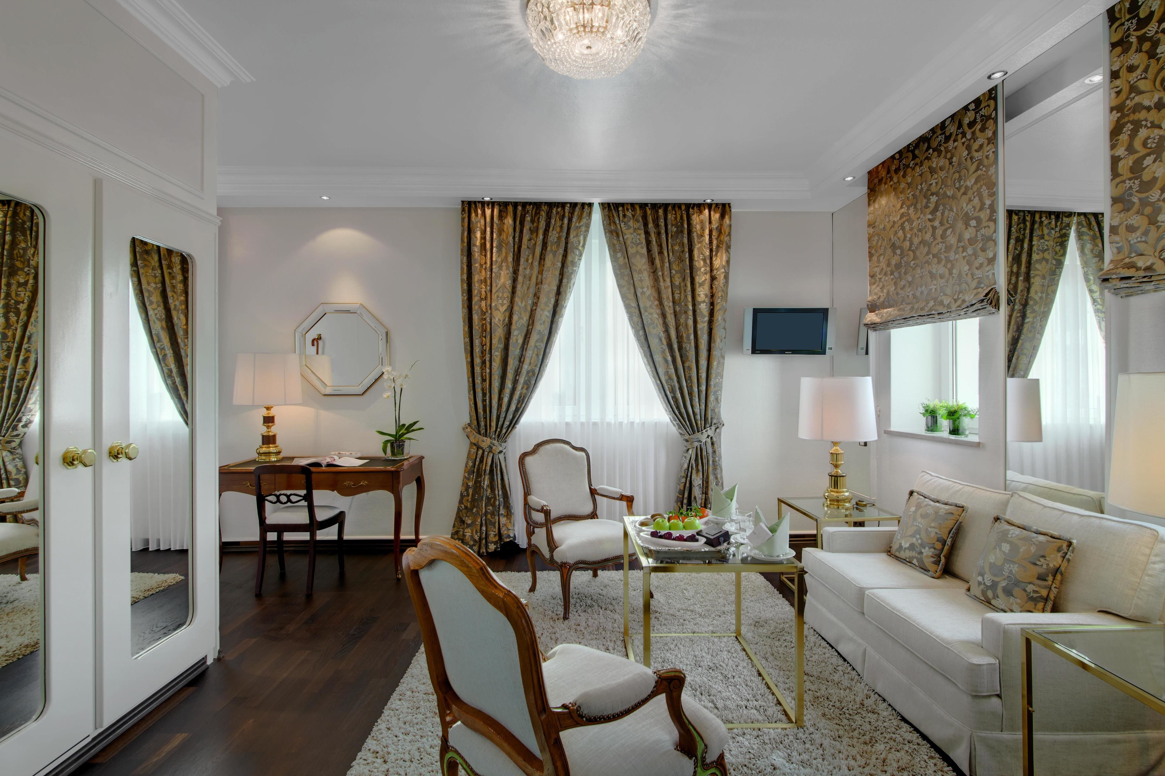 A well-lit, elegantly furnished living room with a sofa, chairs, a desk, and a television.