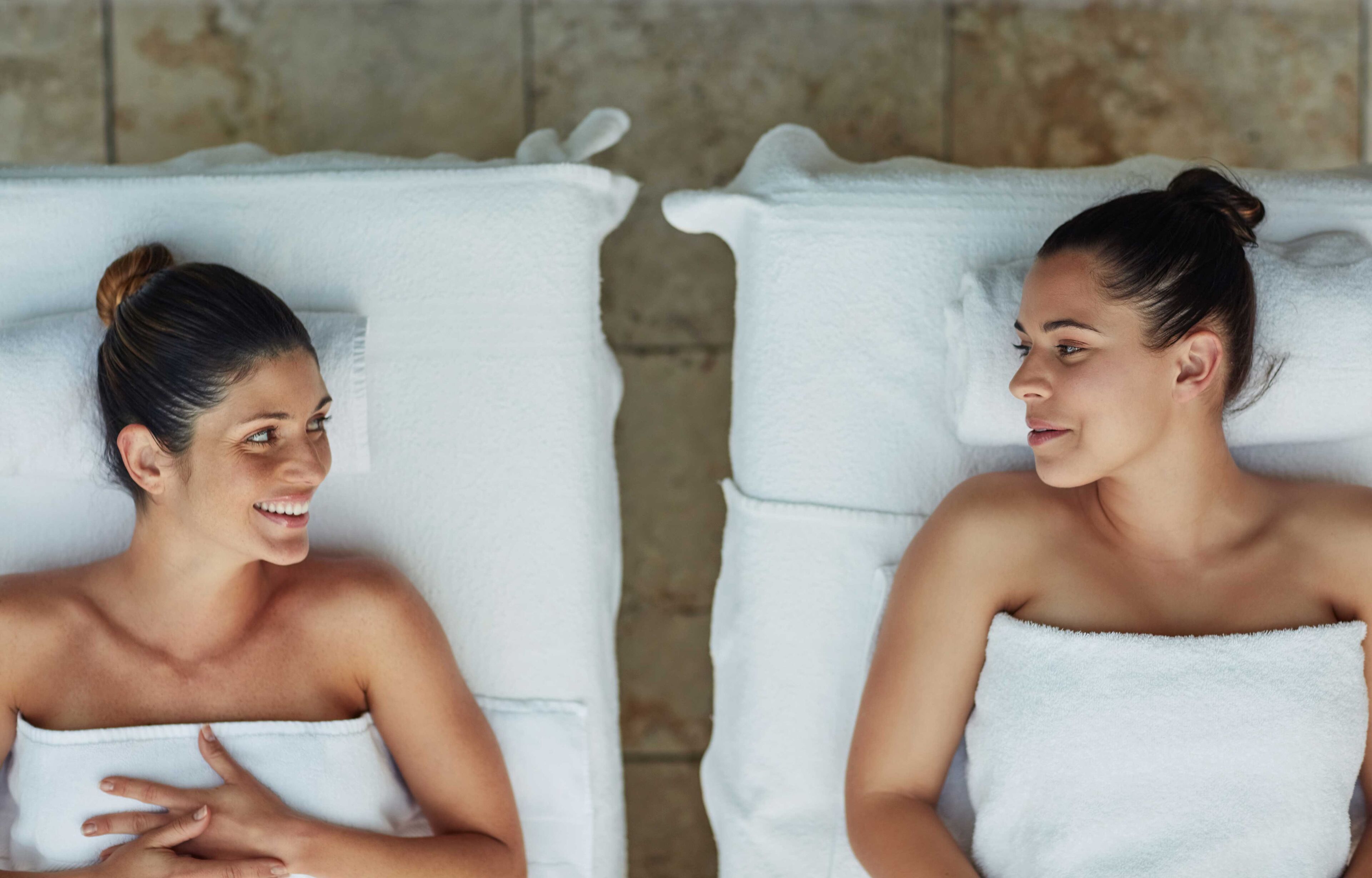 Two spa-style chairs with white towels, set against a stone wall background.
