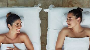Two spa-style chairs with white towels, set against a stone wall background.