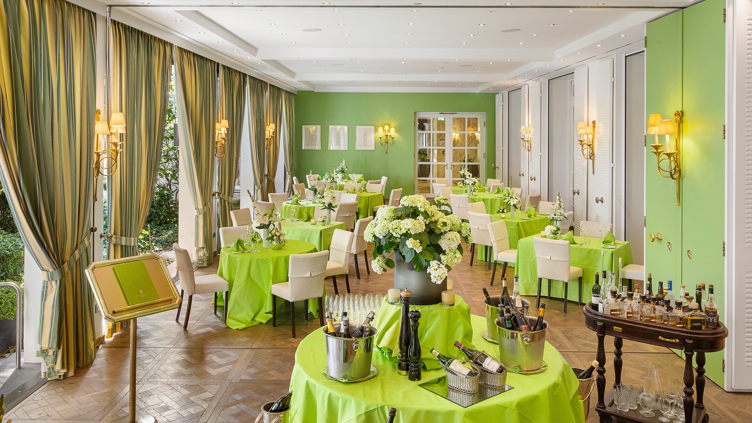 A formal dining room with multiple tables, green tablecloths, and champagne bottles.