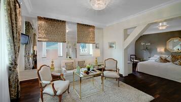 A spacious bedroom with a large bed, a sitting area with chairs, a dining table, and a chandelier.