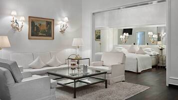 A modern hotel room with a grey sofa set, a glass coffee table, and a bed with white linens.