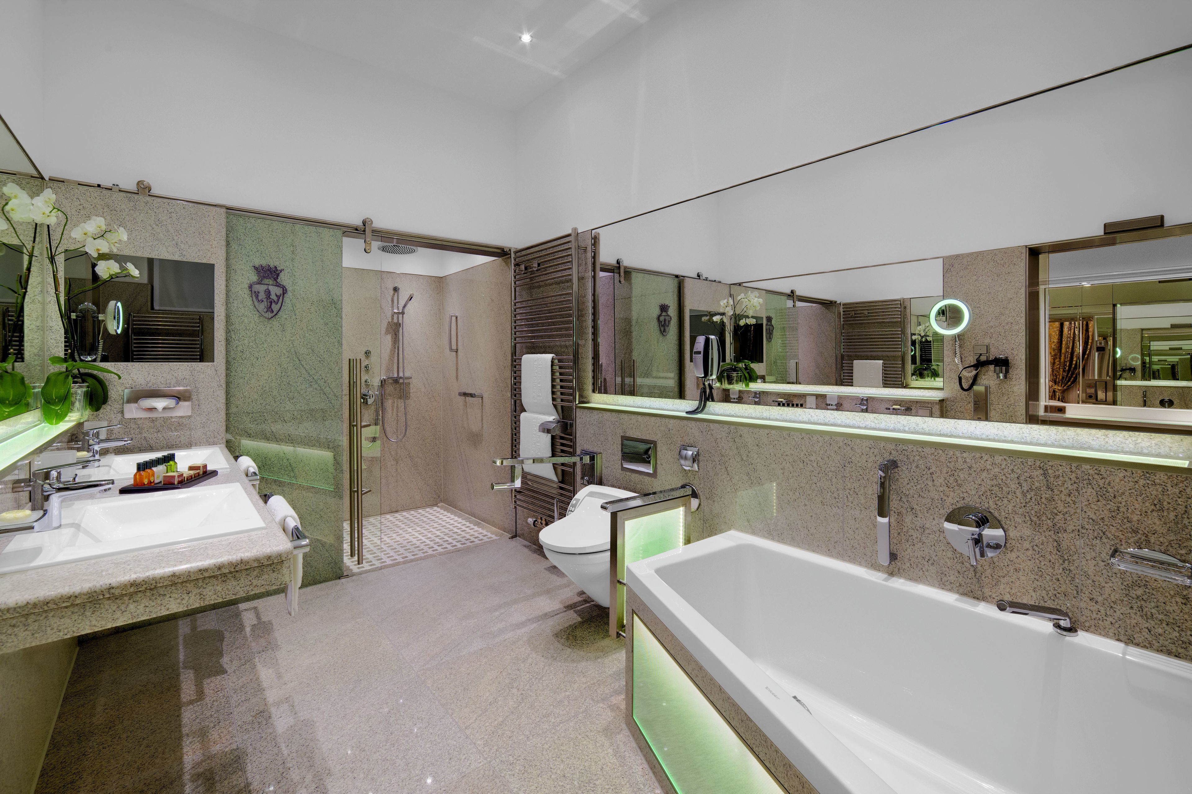A modern bathroom with a large bathtub, two sinks, a toilet, and a shower area.