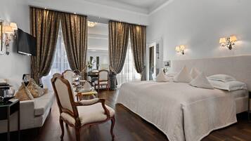 A spacious hotel room with a large bed, a sitting area with a chair and a small table, and a television on the wall.