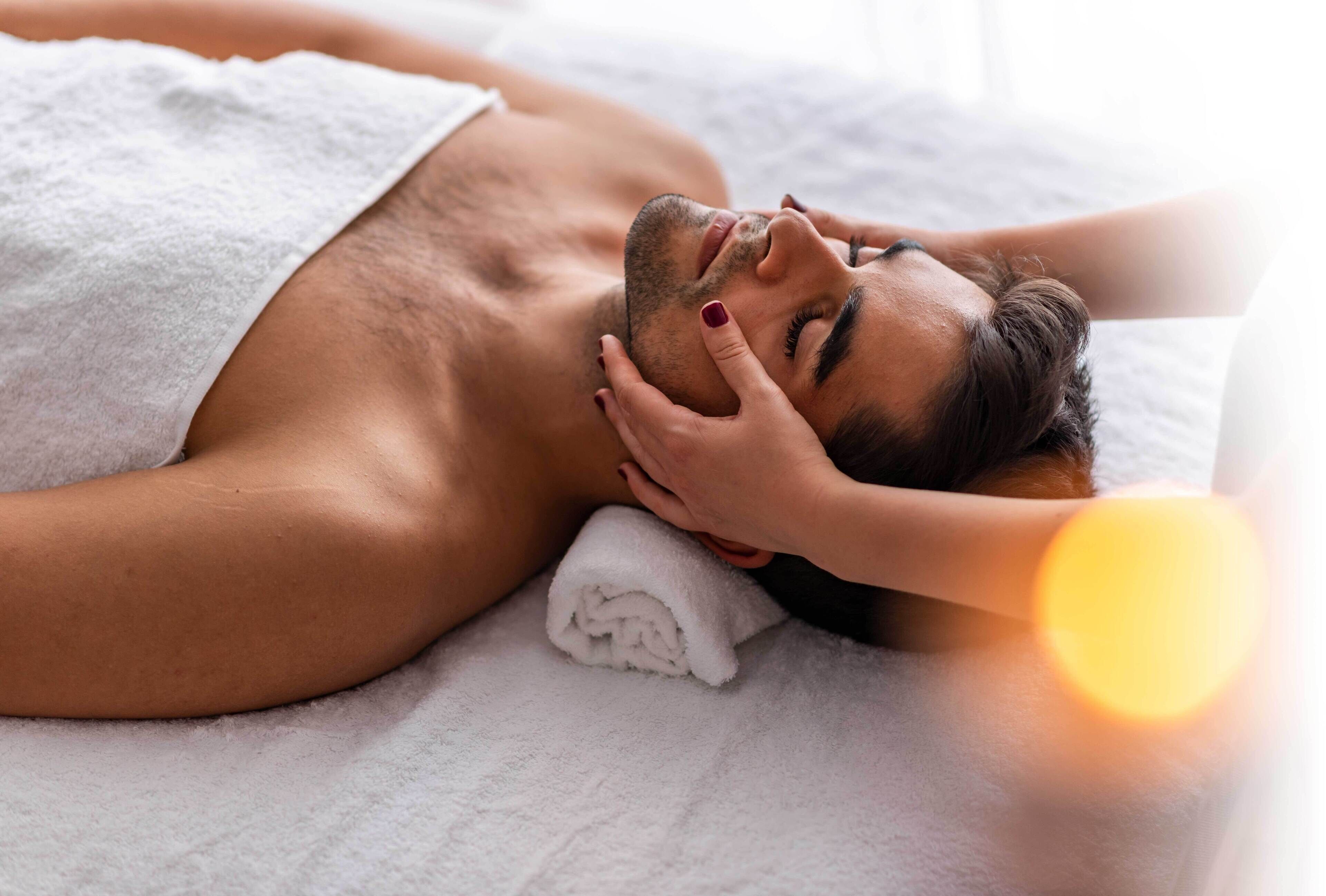 A person lying on a bed with a white towel, a pillow, and a blanket.