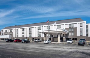 A modern hotel with a flat roof, multiple windows, and a parking lot with several cars.