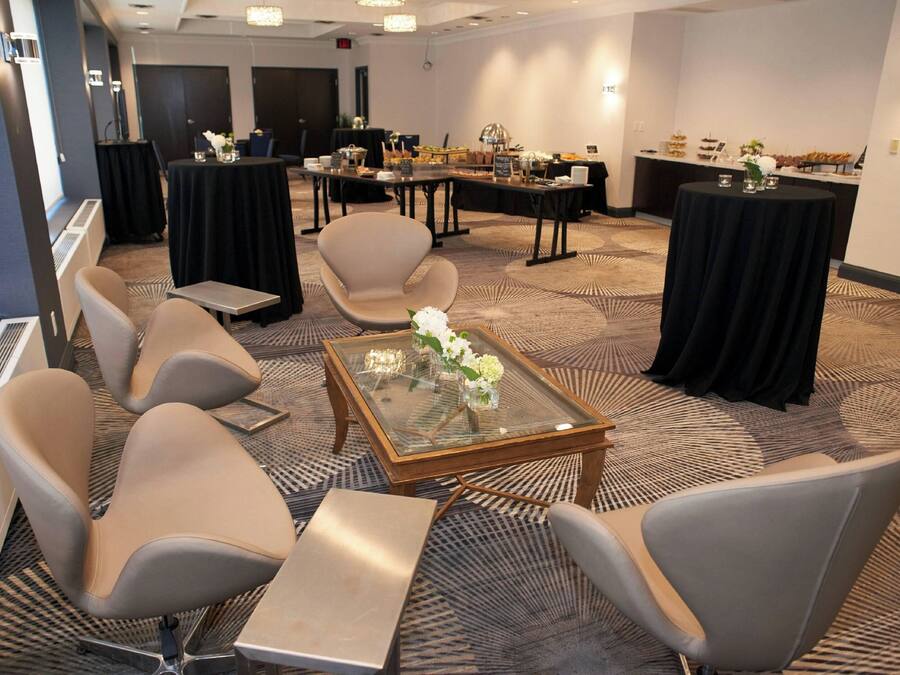 Sala de conferências com mesas redondas, cadeiras e uma mesa de centro de vidro com flores brancas.