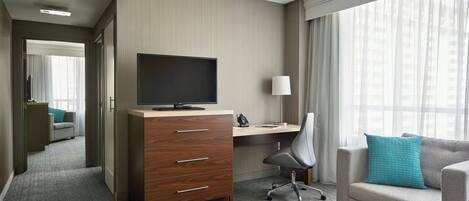 Una habitación de hotel con escritorio, televisor, silla, sofá y ventana con cortinas.