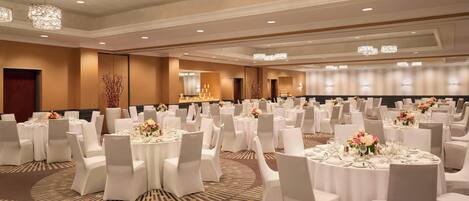 A banquet hall with round tables set for dining, white chairs, and chandeliers.