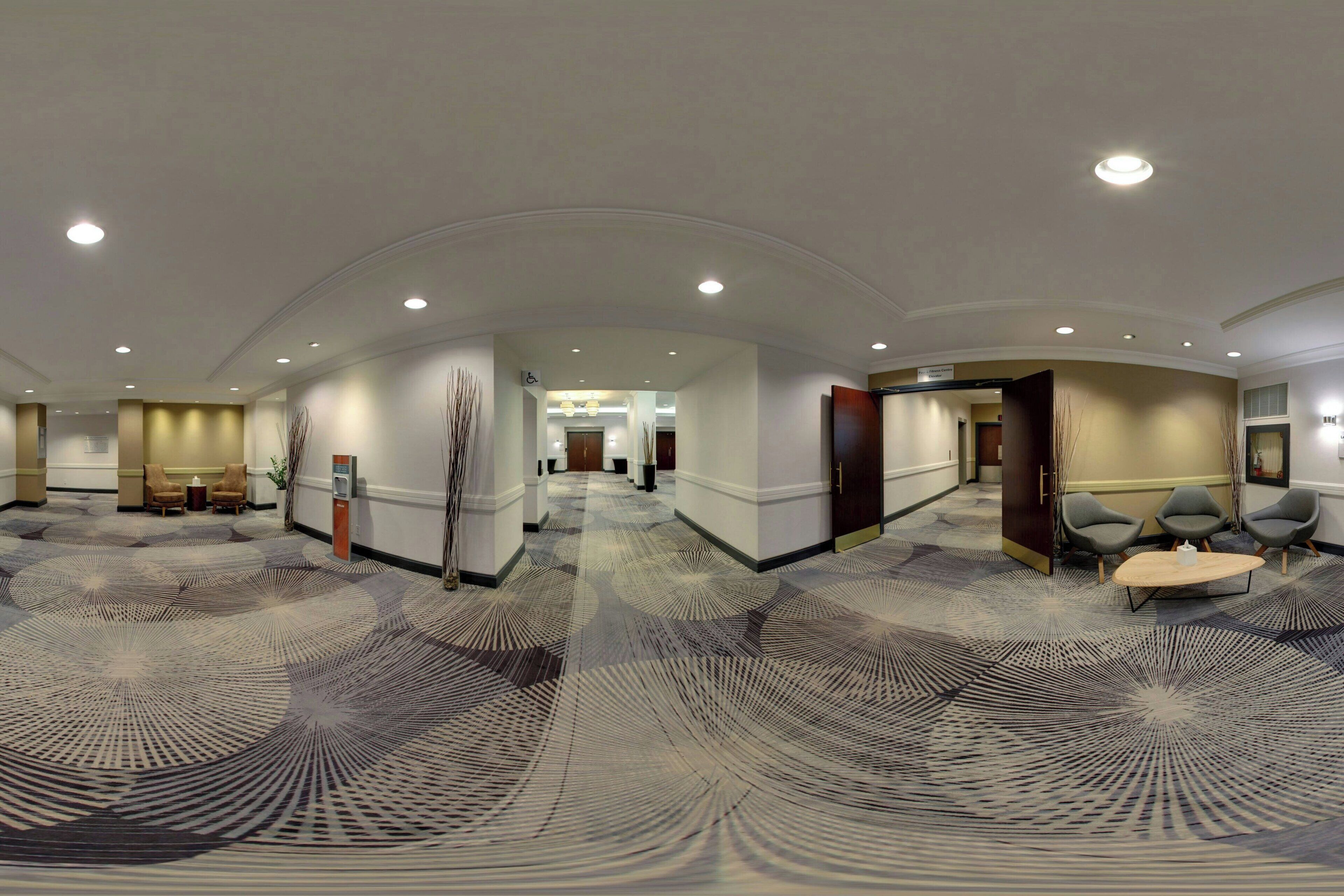 A spacious hotel lobby with a patterned carpet, seating areas, and a reception desk.