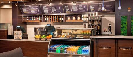 A modern cafe with a counter, menu boards, a beverage display, and seating.