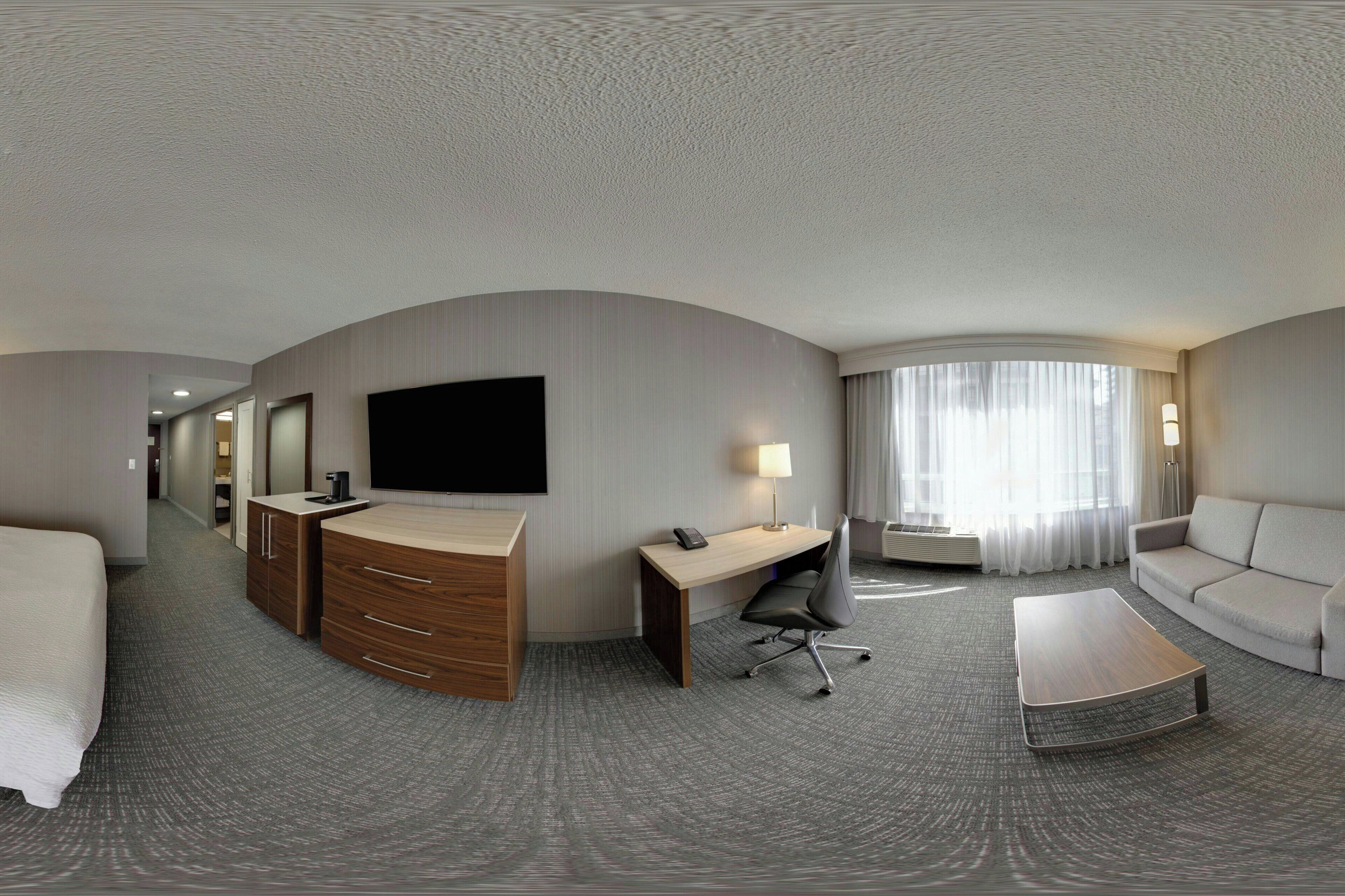 A hotel room with a bed, a desk, a chair, a sofa, a TV, and a window with curtains.