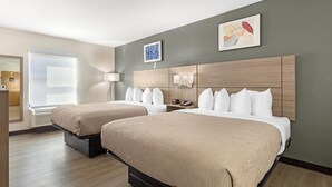 A hotel room with two beds, a large window, a wall-mounted TV, and a painting. - Quality Inn Washington NC (Washington)