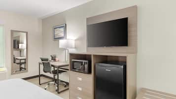 A hotel room with a bed, a desk with a chair, a microwave, a refrigerator, a flat-screen TV, a lamp, and a mirror.