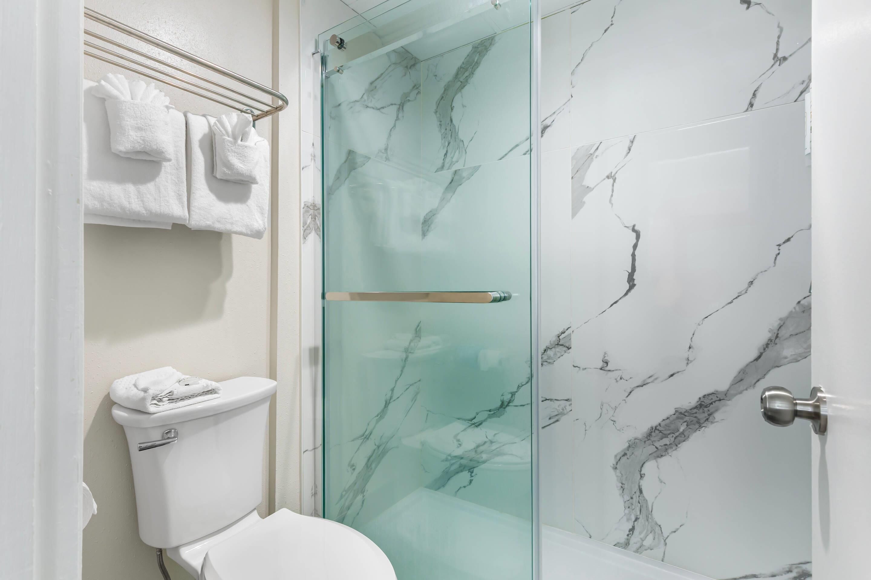 A bathroom with a glass shower enclosure, a toilet, and marble-patterned walls.
