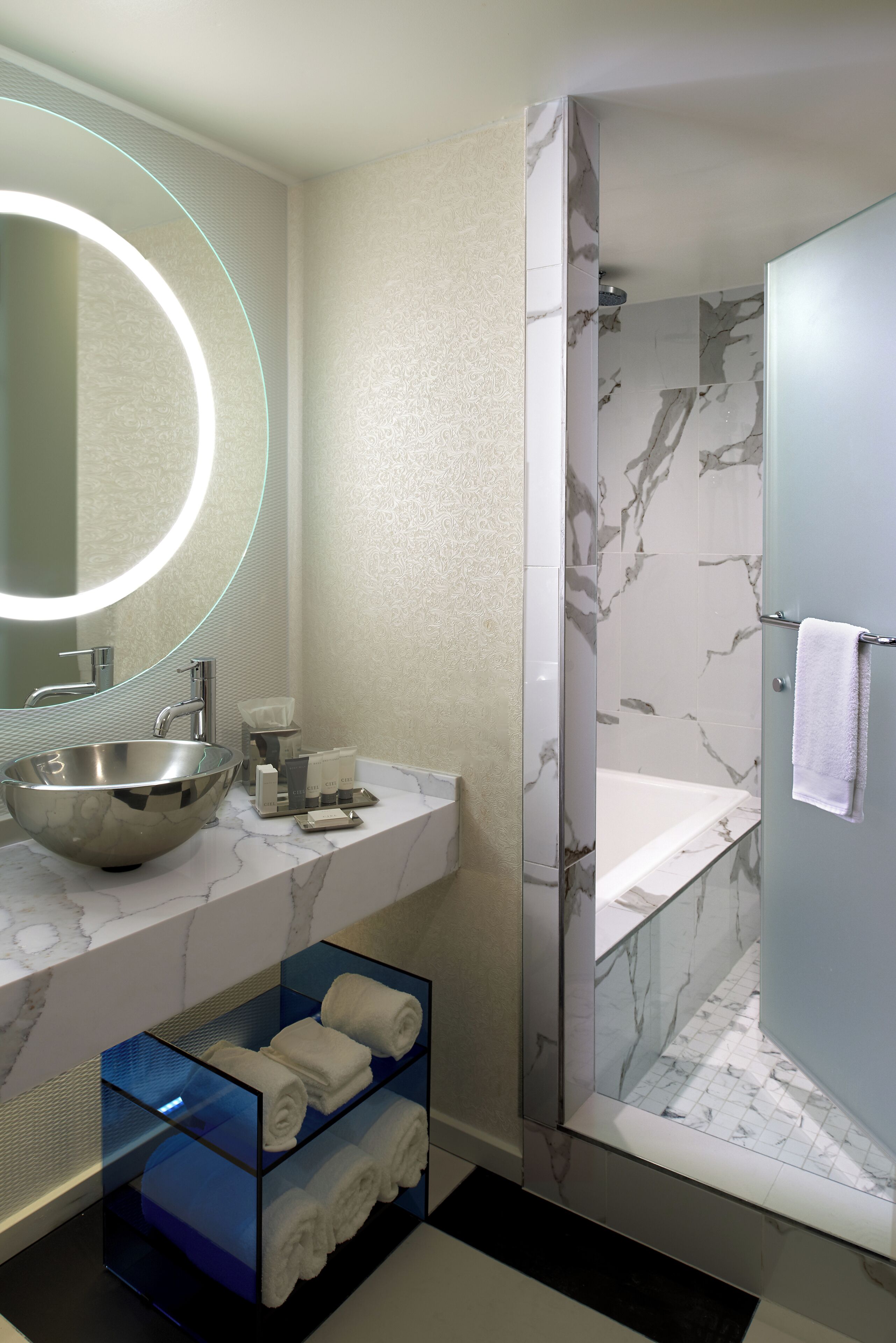 A modern bathroom with a large mirror, a vessel sink, a glass shower enclosure, and a marble-tiled shower area.