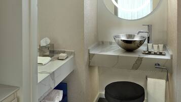 Een badkamer met een ronde spiegel, een waskom, een handdoekhouder en een zwarte kruk.