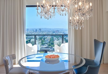 A modern living room with a flat-screen TV, a glass coffee table, a blue armchair, ottomans, and a chandelier. at The Valorian Los Angeles, Curio Collection by Hilton
