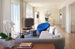 A modern living room with a sofa, a blue chair, a television, and a chandelier. - The Valorian West Hollywood, Curio Collection by Hilton (West Hollywood)