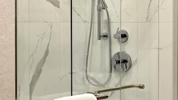 Une douche fermée par des parois en verre, dotée d’un pommeau de douche à main et d’une barre avec une serviette blanche.