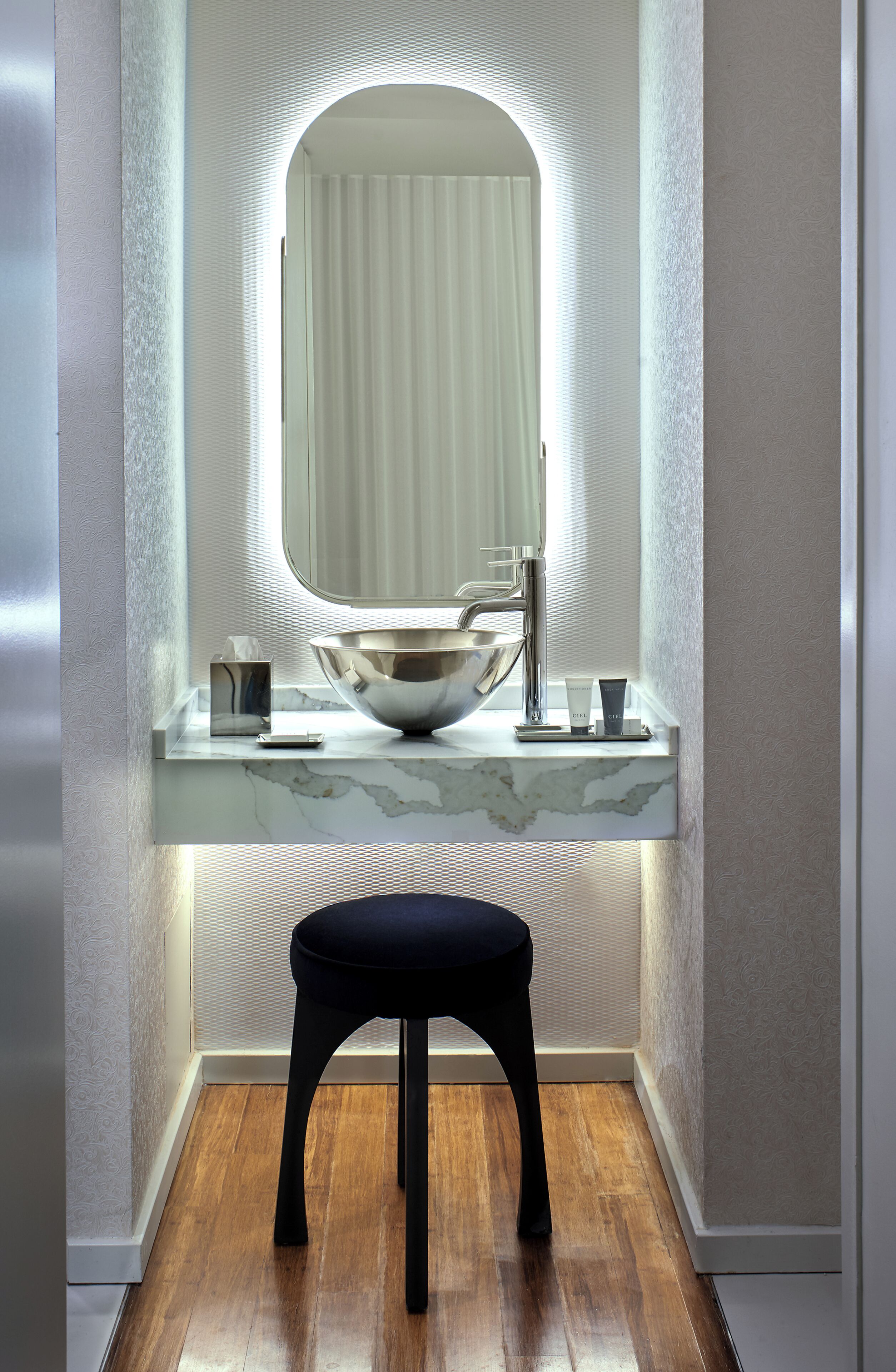 Une salle de bain moderne avec un meuble-lavabo en marbre, un grand miroir et un tabouret noir.