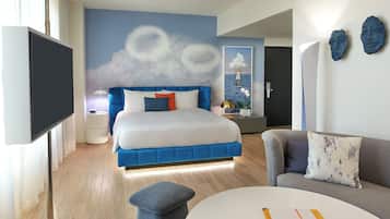 Una habitación de hotel moderna con una cama, un sofá, un televisor y una pared con un mural de nubes.