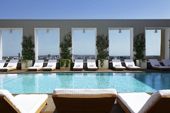 A modern living room with a round sofa, a blue chair, a white table, and a large window with curtains. at The Valorian Los Angeles, Curio Collection by Hilton