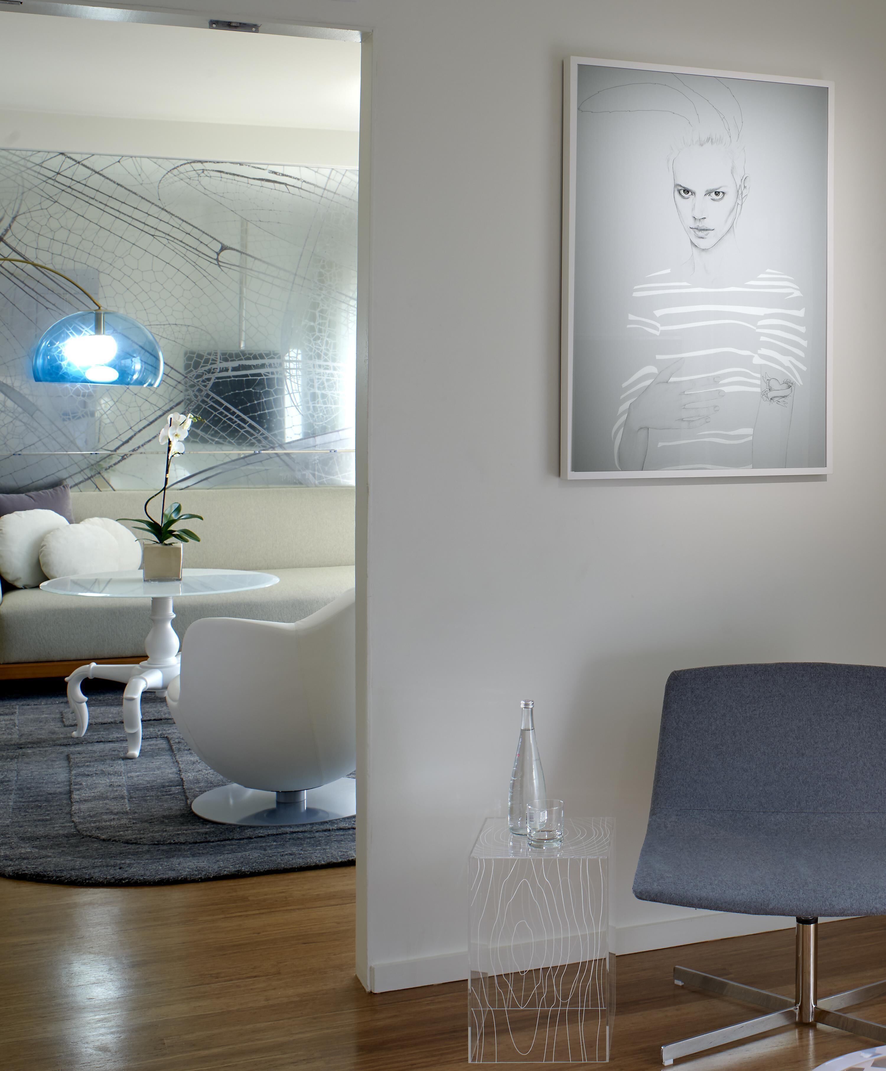 A modern living room with a white sofa, a glass coffee table, a white armchair, a clear glass sculpture, and a framed abstract artwork on the wall.