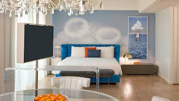 A modern bedroom with a large bed, a TV, a glass table with oranges, and a wall mural.