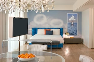 Un dormitorio moderno con una cama grande, un televisor, una mesita de vidrio con naranjas y un mural en la pared.
