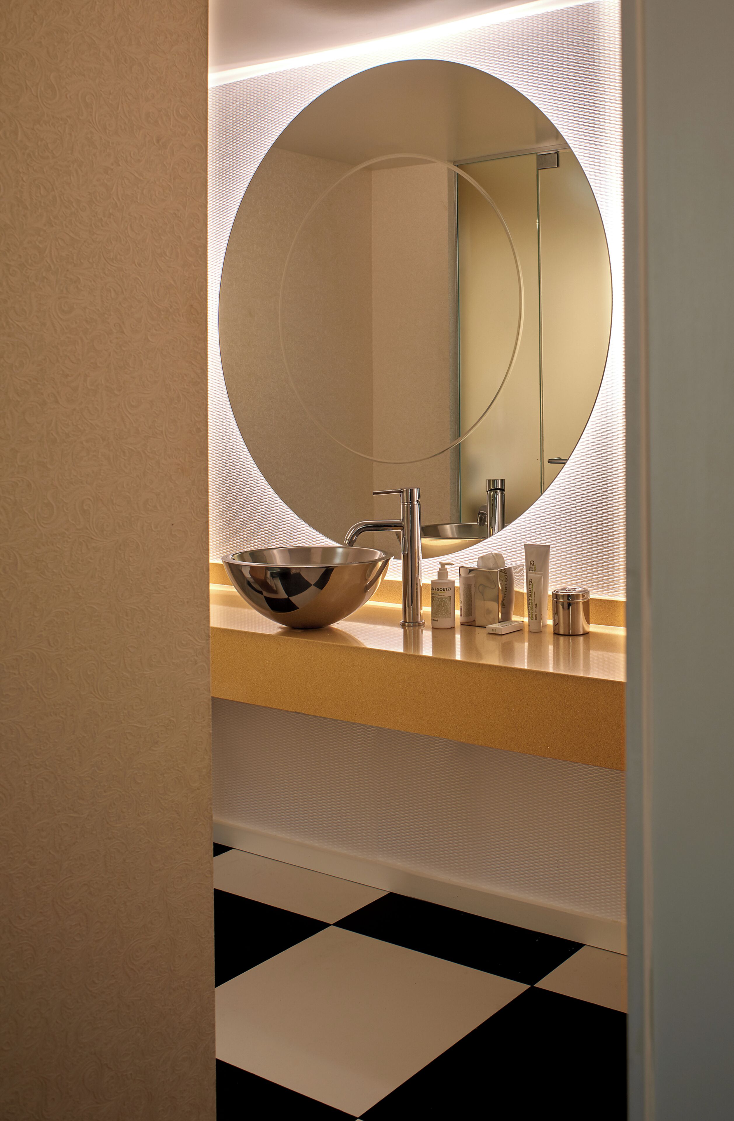 Une salle de bain avec un miroir rond, un lavabo en forme de coupe et des articles de toilette posés sur le comptoir.
